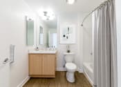 Thumbnail 28 of 104 - A white toilet sits in a bathroom next to a sink and a shower at The Grand Apartments, Oakland 94612